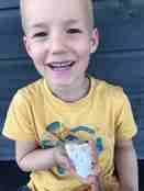Nærbilde av blond gutt på fem år med stort smil og blekksprutskall i hendene 