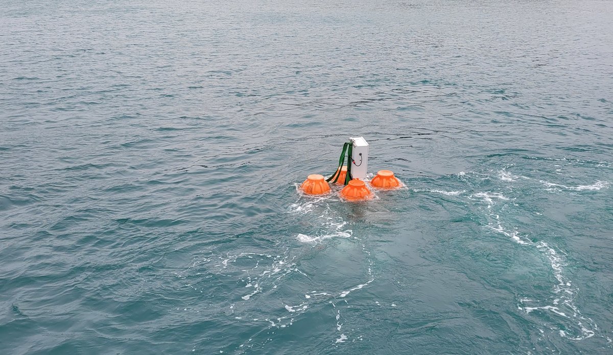 
Grå metallboks med oransje flyteelementer på hver side flytende i sjøen.