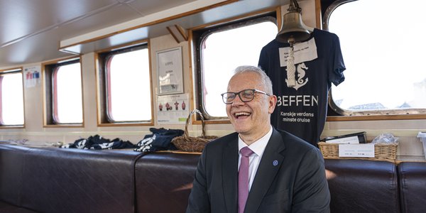 

En mann i dress og med briller sitter inne i en liten passasjerbåt.