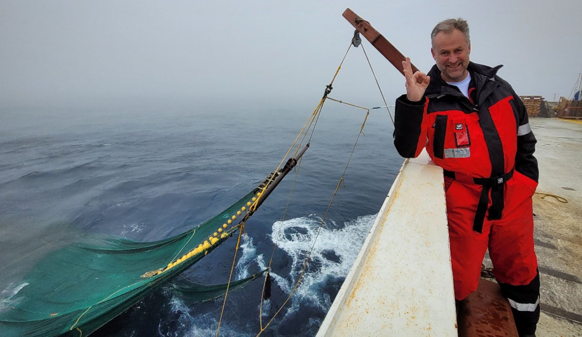 
mann på skip med tommel opp, trål hengende ut i havet bak