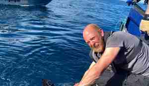 Fritidsfisker Andre Starkenberg hjelper til å holde håbrannen han selv fikk på kroken inntill båten mens merkingen pågår. Han holder i et sterkt tau som er festet rundt haiens buk.