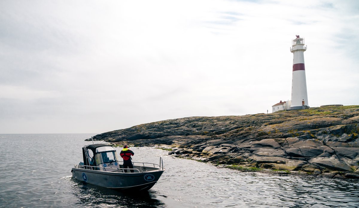 
Liten båt i forgrunnen og stort, hvitt fyrtårn på holme i bakgrunnen.