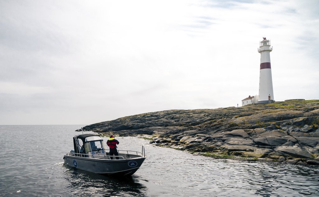 Liten båt i forgrunnen og stort, hvitt fyrtårn på holme i bakgrunnen.