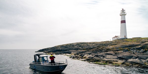 

Liten båt i forgrunnen og stort, hvitt fyrtårn på holme i bakgrunnen.