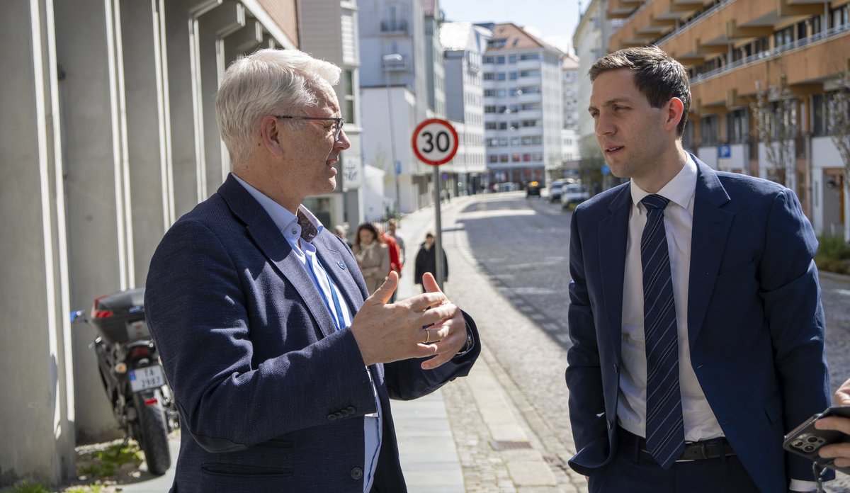 
To dresskledde menn står utenfor et bygg i solskinn