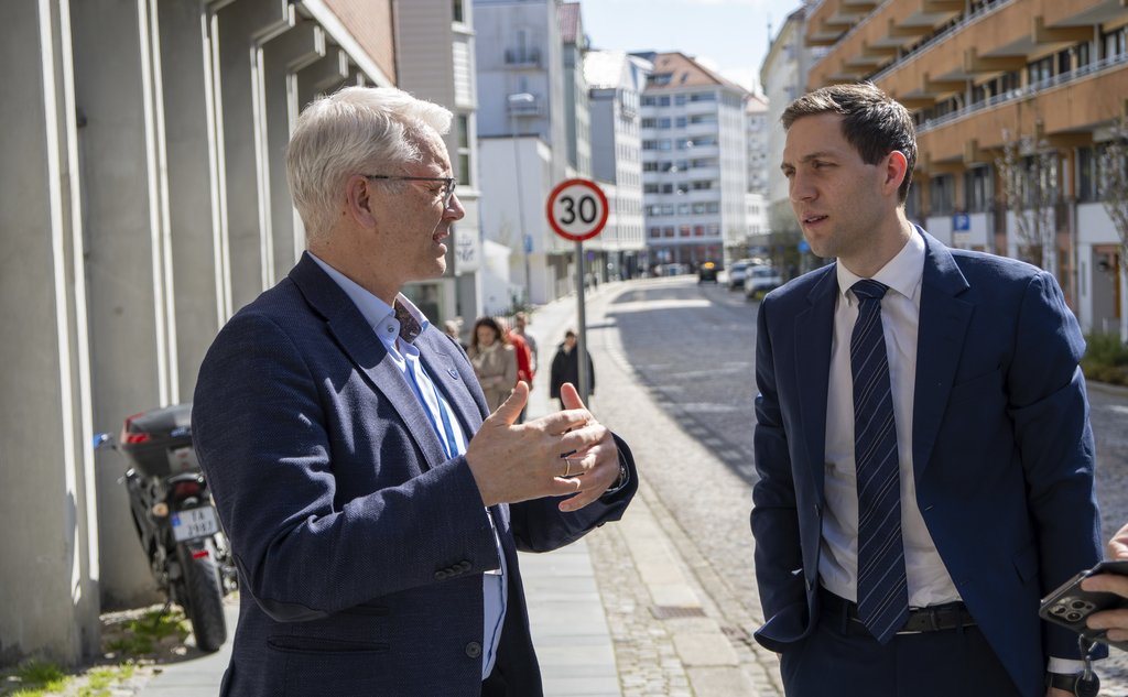 To dresskledde menn står utenfor et bygg i solskinn