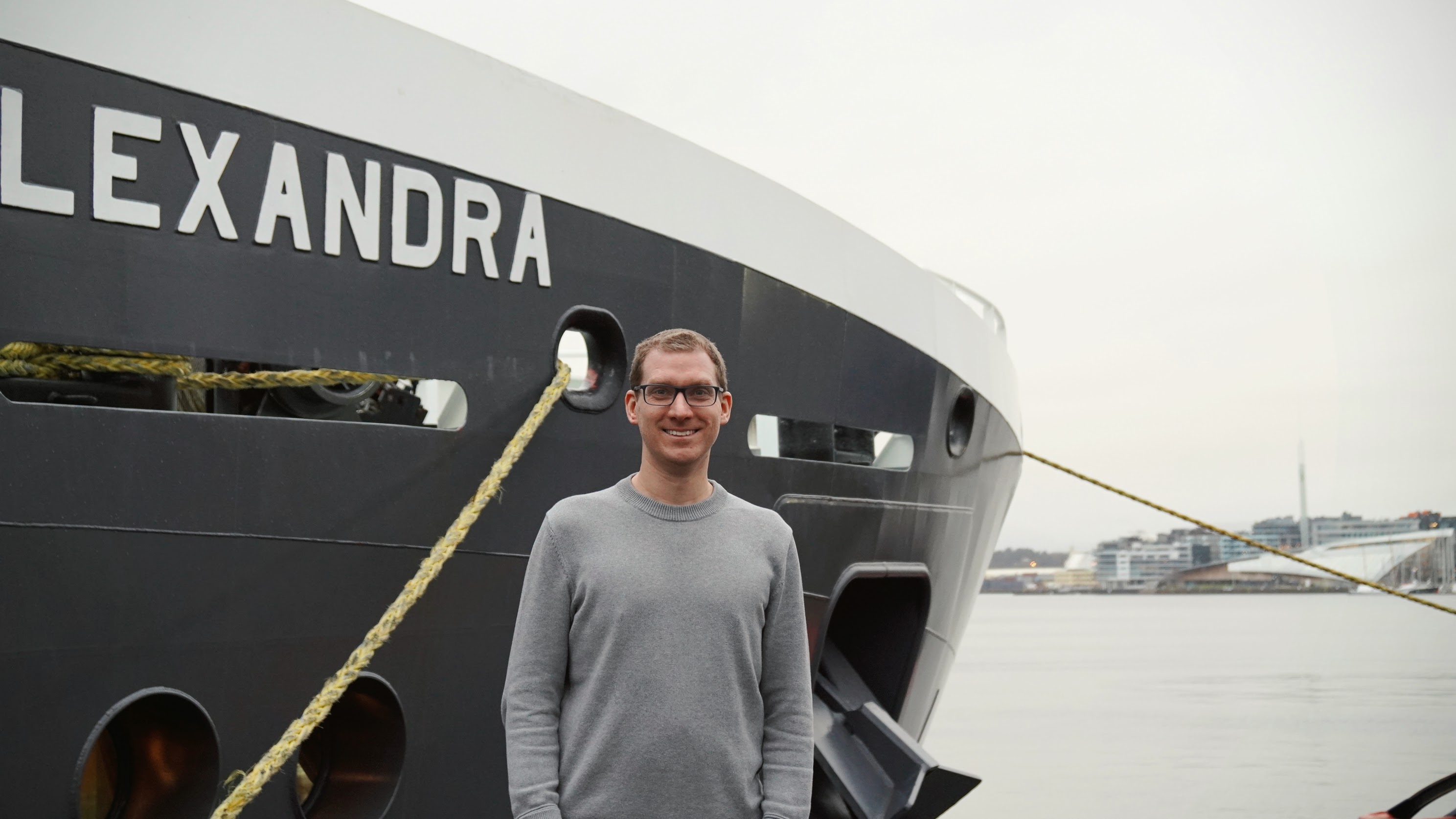 foto av mann foran baugen på en båt. Tjuvholmen skimtes i bakgrunnen