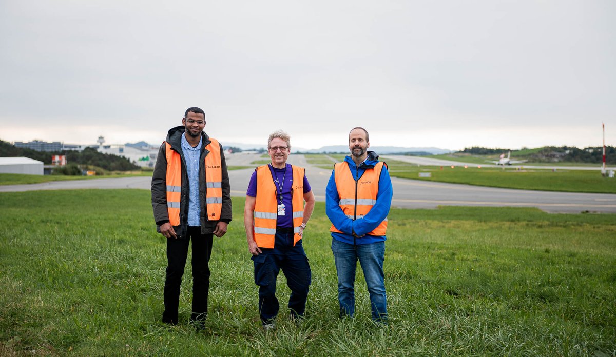 
tre menn i oransje vest på rullebanen på Flesland.