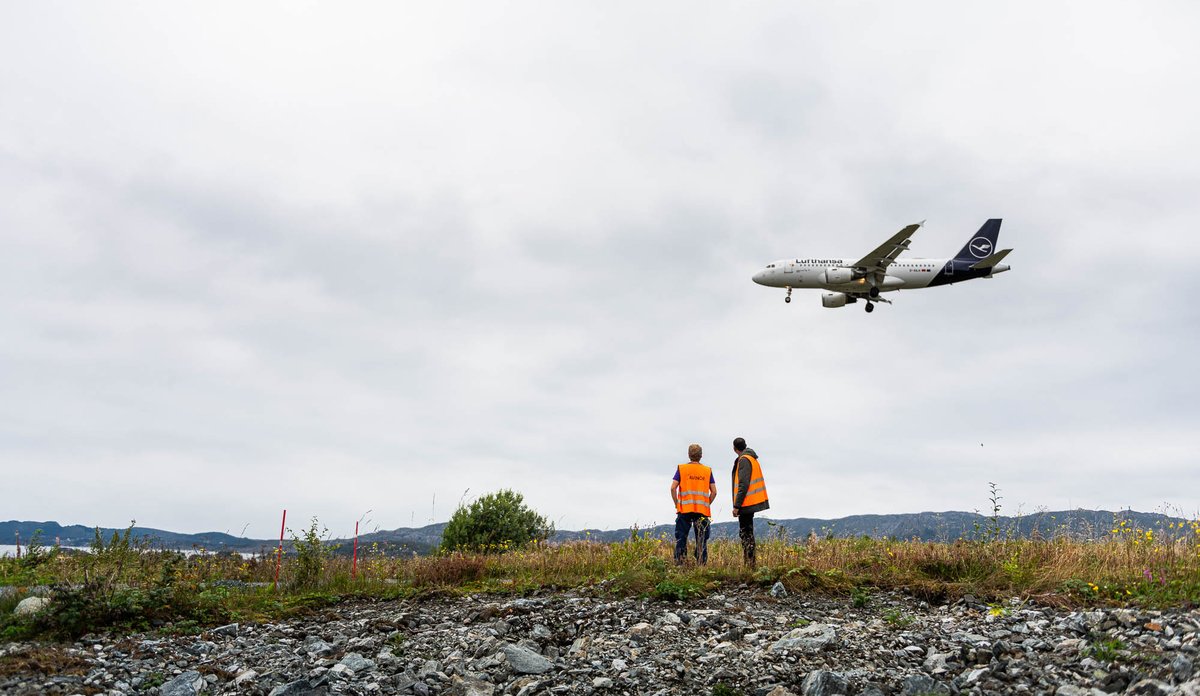 menn i oransje vest med fly i bakgrunnen