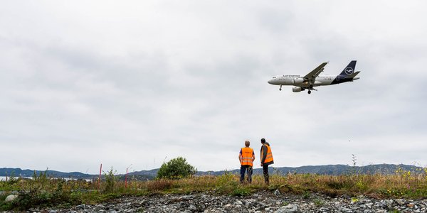 

tre menn i oransje vest på rullebanen på Flesland.