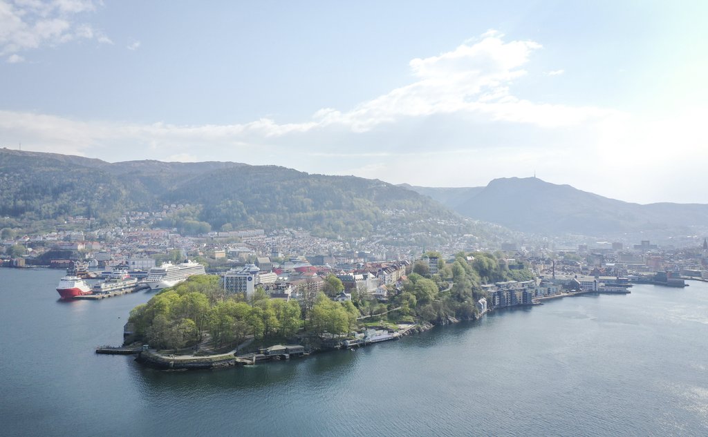 Oversiktsbilde som viser halvøy med grønne trær, by og fjell i bakgrunnen.