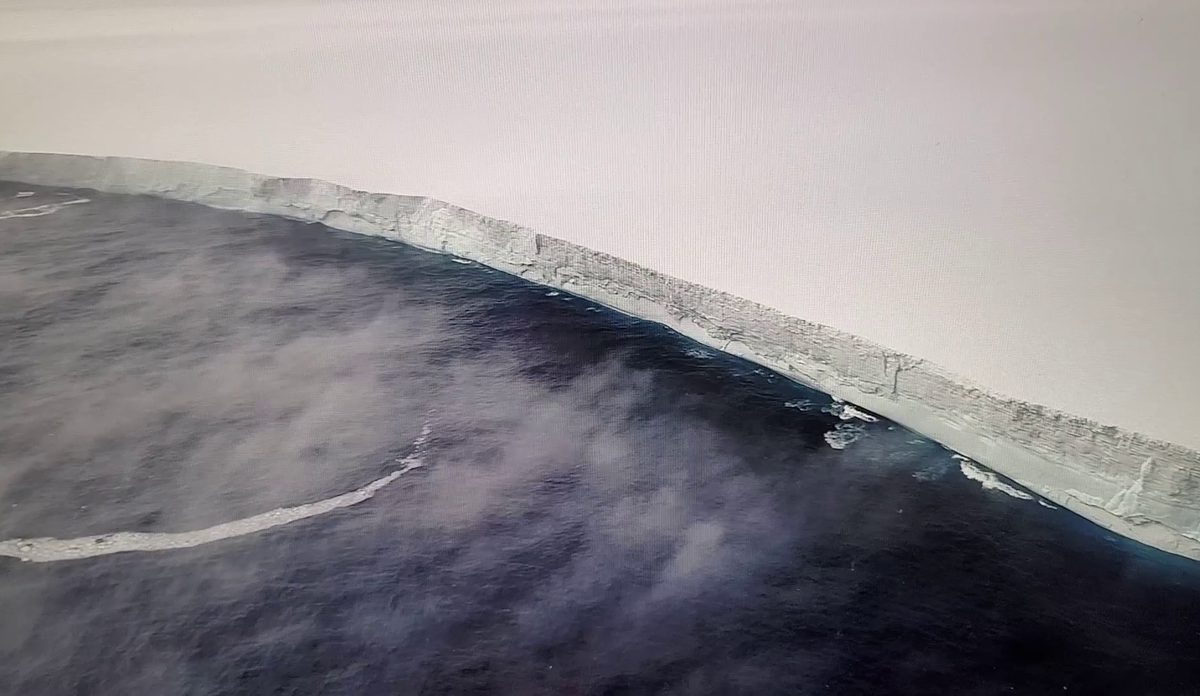 Enormt stort isfjell møter havet, sett fra fugleperspektiv 