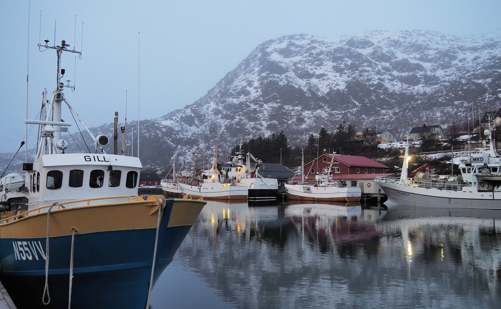 fiskebåter liggende langs kaien, med snøkledd fjell i bakgrunnen