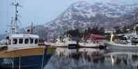 

fiskebåter liggende langs kaien, med snøkledd fjell i bakgrunnen