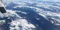 

Fjord omgitt av snøkledde fjell sett ovenfra fra et fly med deler av propell i forgrunnen.