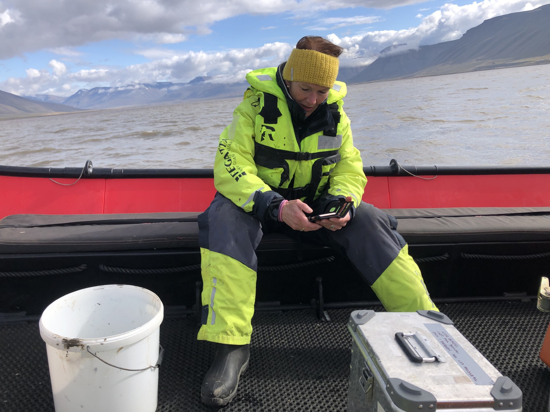 En kvinnelig forsker sitter i en båt. Hun samler sedimentprøver fra fjorden