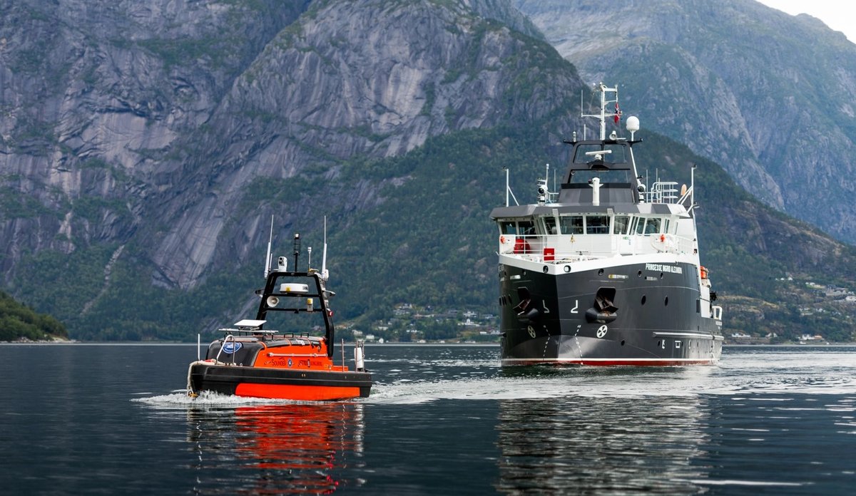 
En oransje ubemannet farkost og et forskningsfartøy i vannet med fjell i bakgrunnen.