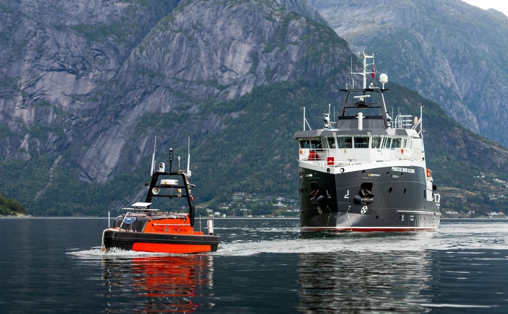 En oransje ubemannet farkost og et forskningsfartøy i vannet med fjell i bakgrunnen.
