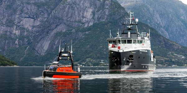 

En oransje ubemannet farkost og et forskningsfartøy i vannet med fjell i bakgrunnen.