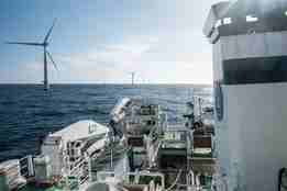 dekk på forskningsfartøy ute på havet i sol med vindturbiner i horisonten