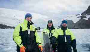 Tre personer smiler mot kamera, godt kledde, i båt med is på alle kanter rundt 