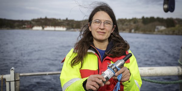 

kvinne i kjeledress i båt holder en avlang ting mot kamera