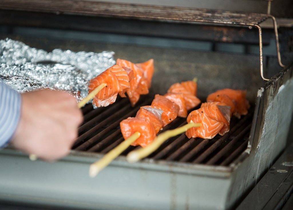 Grillspyd med laks blir lagt på grillen.