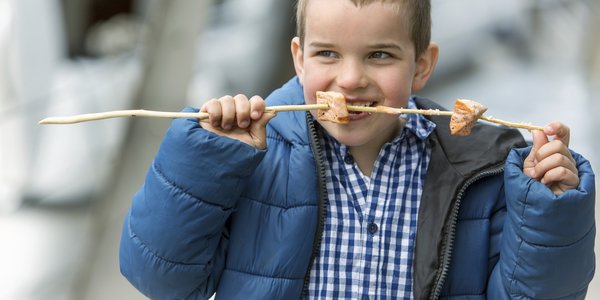 

Liten gutt med blå jakke spiser grillede lakseterninger tredd på en pinne.