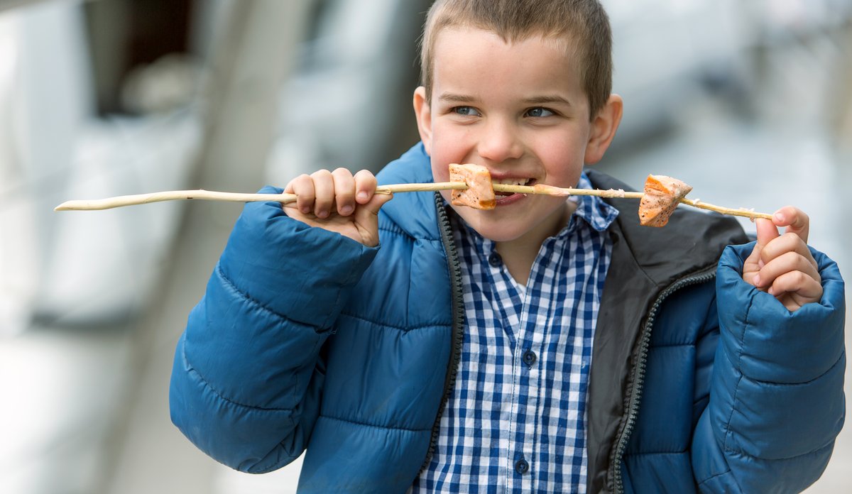 Foto av gutt  som spiser laks av grillspyd