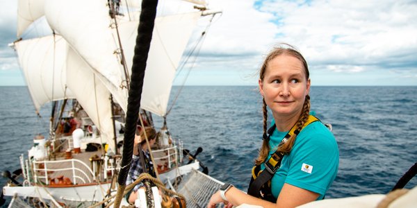 

foto av kvinne i baugspydet på seilskip, med skipet i bakgrunnen