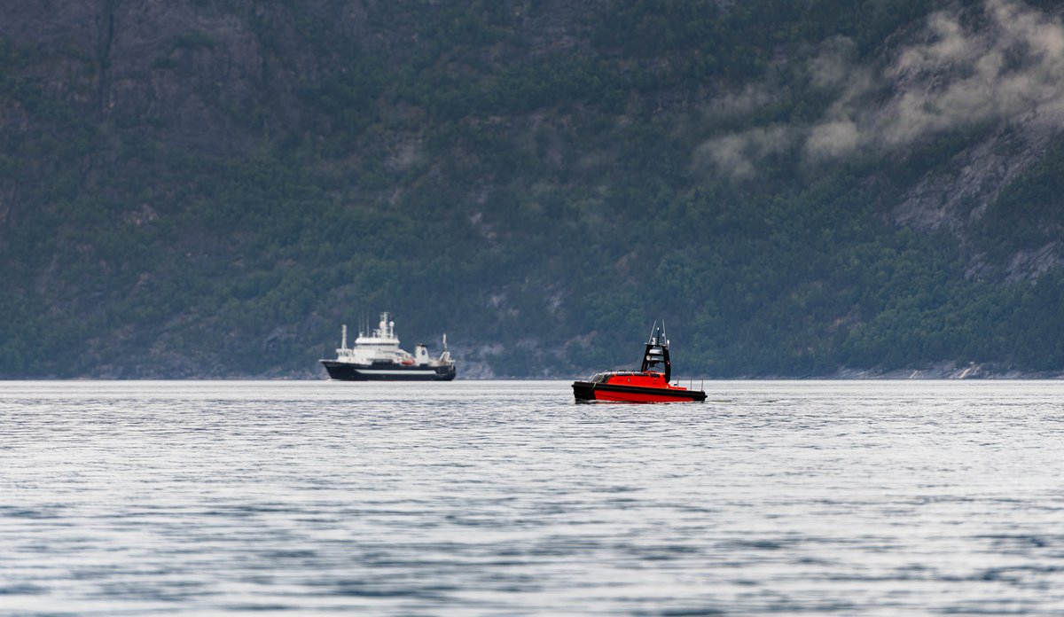 
Foto av en fjord med forskingsfartøy og liten båt-liknende drone i forgrunnen, i en fjord.
