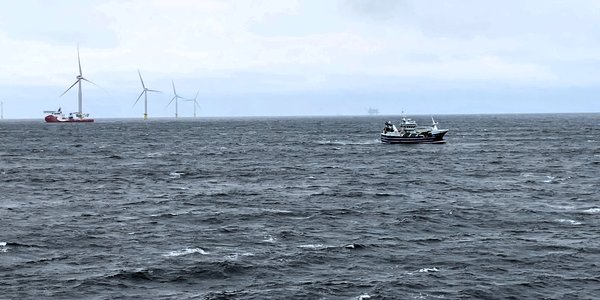 

Fiskebåt passerer vindturbiner i hav med skummende bølger 