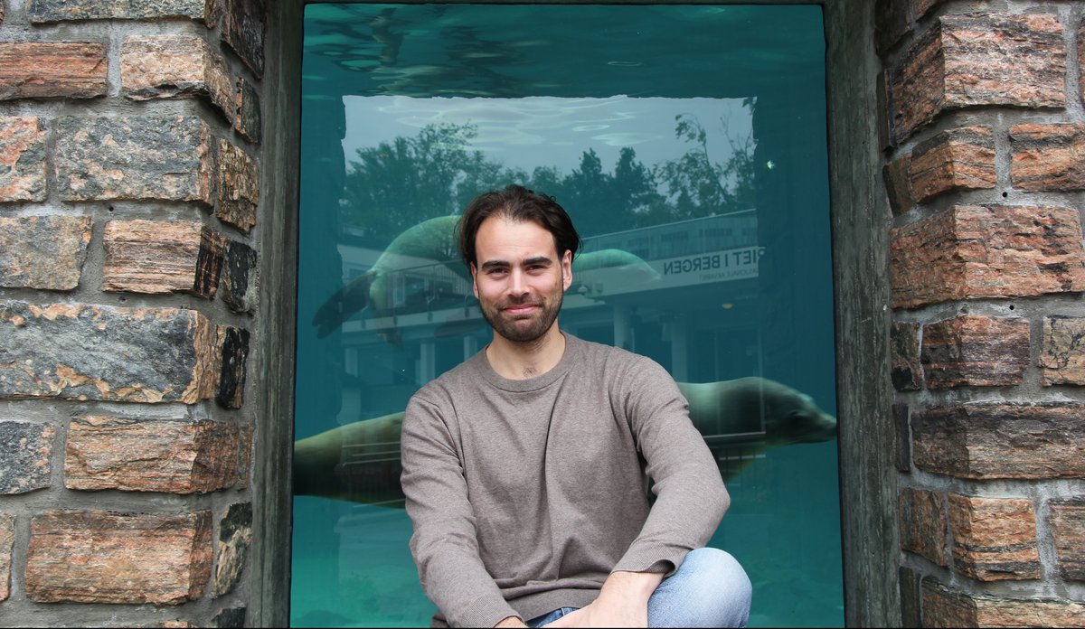 
Håvard Brügger Helgesen på Akvariet med en sel svømmende bak ryggen sin