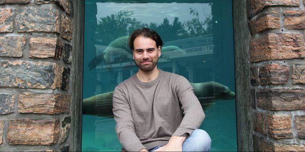Håvard Brügger Helgesen på Akvariet med en sel svømmende bak ryggen sin