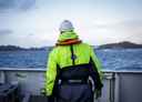 Havforskar i kjeledress på båt på fjorden, han står med ryggne til.