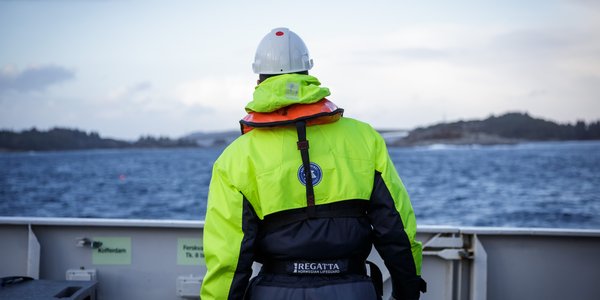 

Havforskar i kjeledress på båt på fjorden, han står med ryggne til.