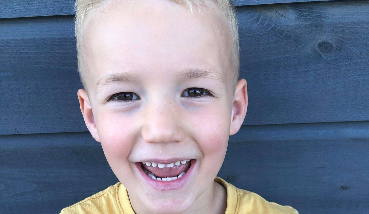 
Nærbilde av smilende gutt på fem år, med blondt år og ifølrt gul t-skjorte. 