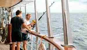 To menn står med en fiskestang over rekka