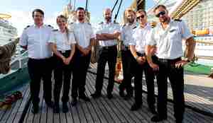 Syv personer med sjømannsuniform med hvit skjorte og mørke bukser står på rekke for fotografen.