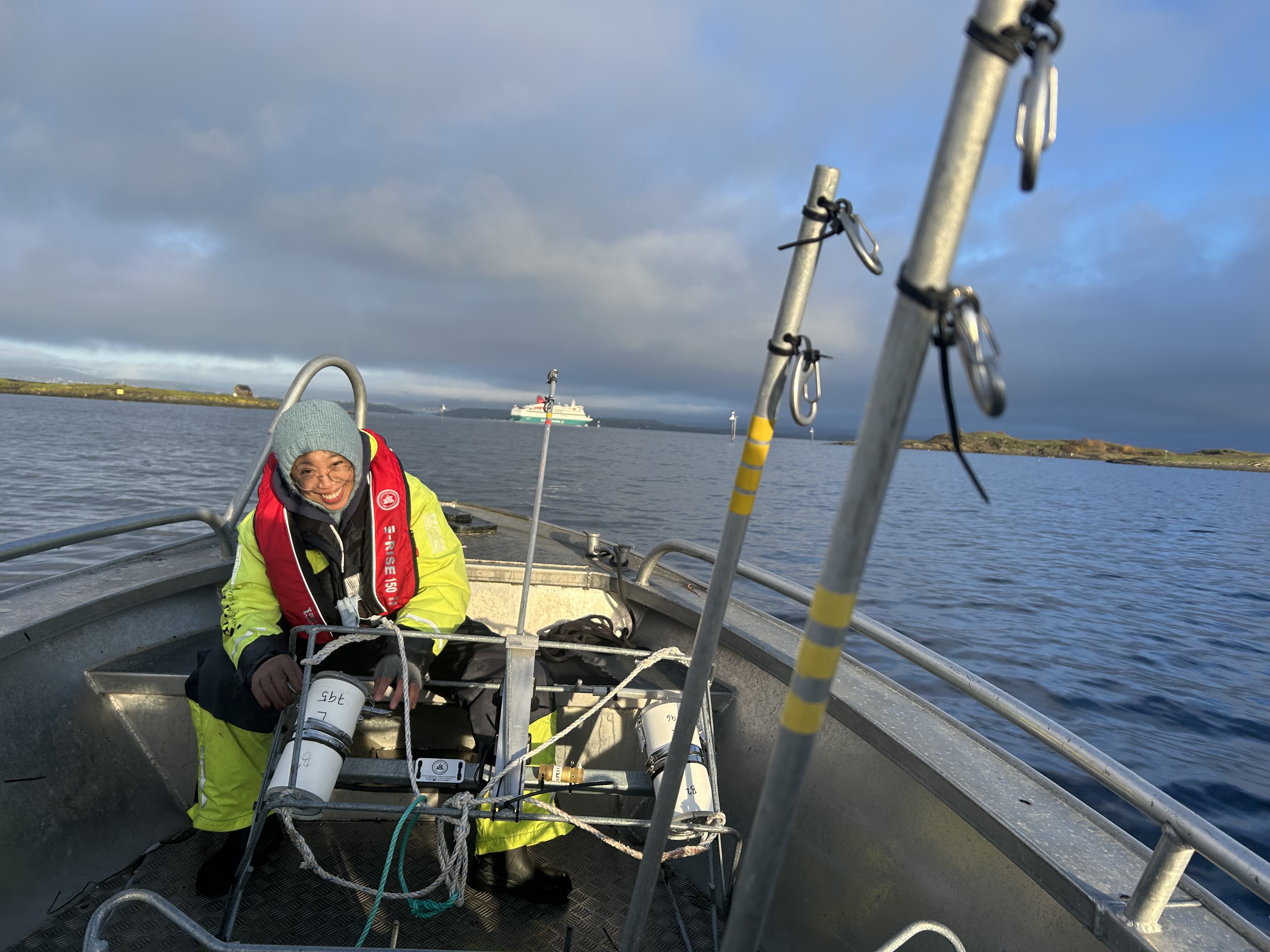 En forsker sitter bak i en båt, som er ute på feltarbeid. Forskeren ser på et kamera