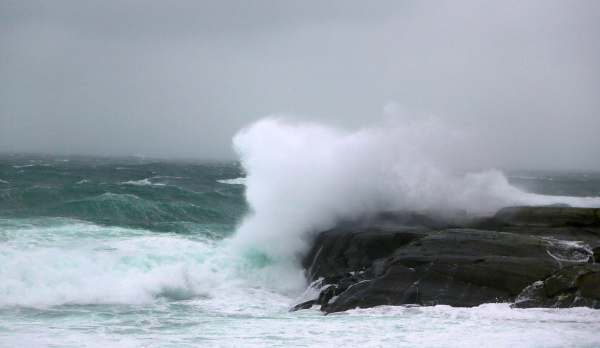 
Bølger som slår mot svaberg så sjøsprøyten står. Opprørt hav og grå himmel i bakgrunnen.