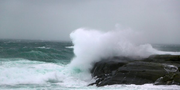 

Bølger som slår mot svaberg så sjøsprøyten står. Opprørt hav og grå himmel i bakgrunnen.