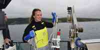 

Stipendiat Johanna holder opp utstyr for å ta vannprøver med, om bord på en båt. 
