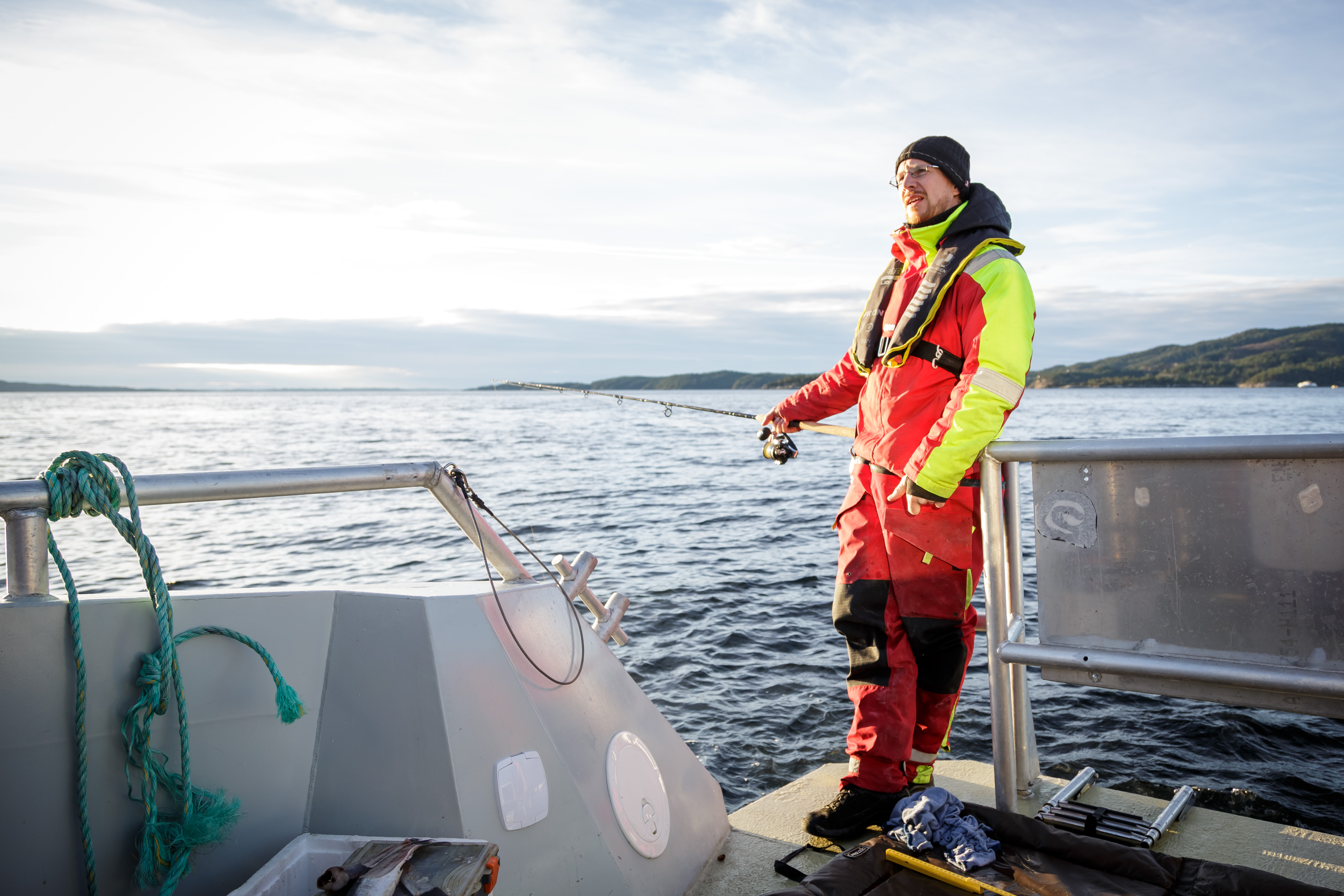 Mann står og slapper av i en båt mens han holder en fiskestang