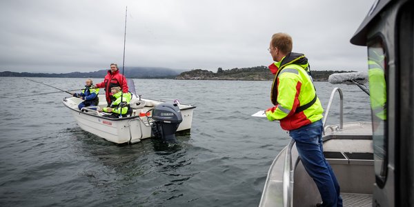 

Mann i en båt holder notatblokk i hendene mens han snakker med tre fiskere i en annen båt.