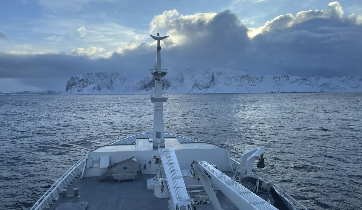 foto av baugen på en båt foran snødekte fjell