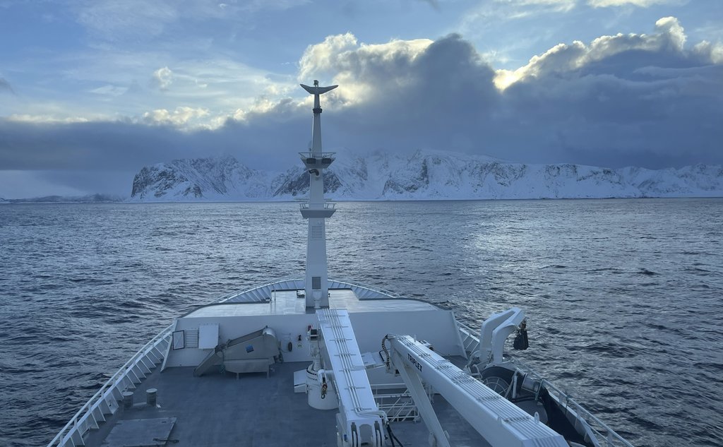 foto av baugen på en båt foran snødekte fjell