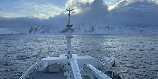

foto av baugen på en båt foran snødekte fjell