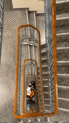 En smal trappeoppgang. Helt i bunnen av trappen står en målerigg med ekkolodd, som lyser mot en blink som henger i 6. etasje. 