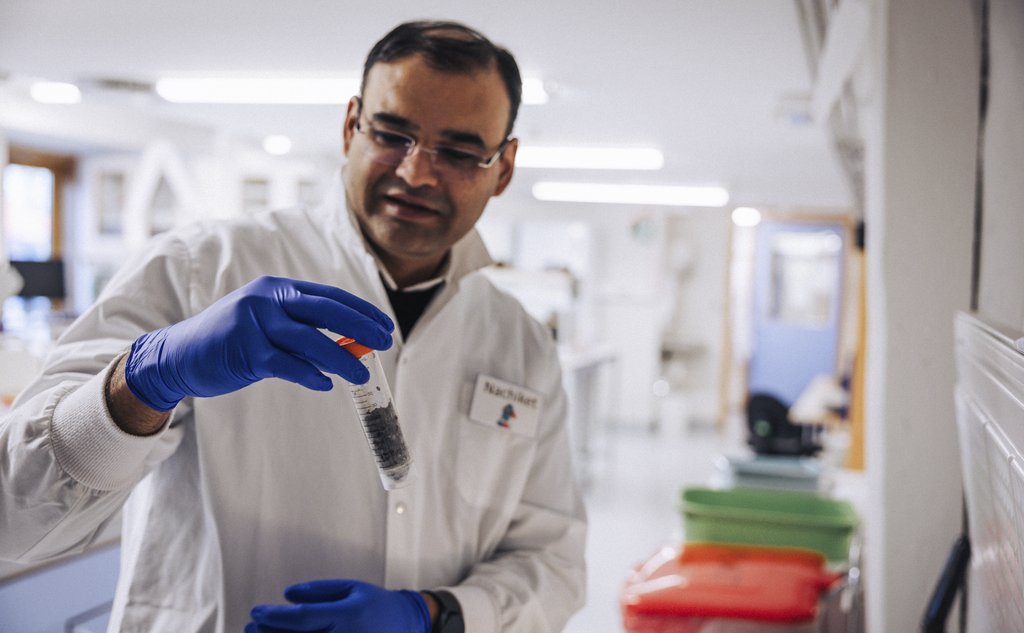 En mannlig forsker i hvit frakk er på et laboratorie. I hånden holder han et rør med en sedimentprøve